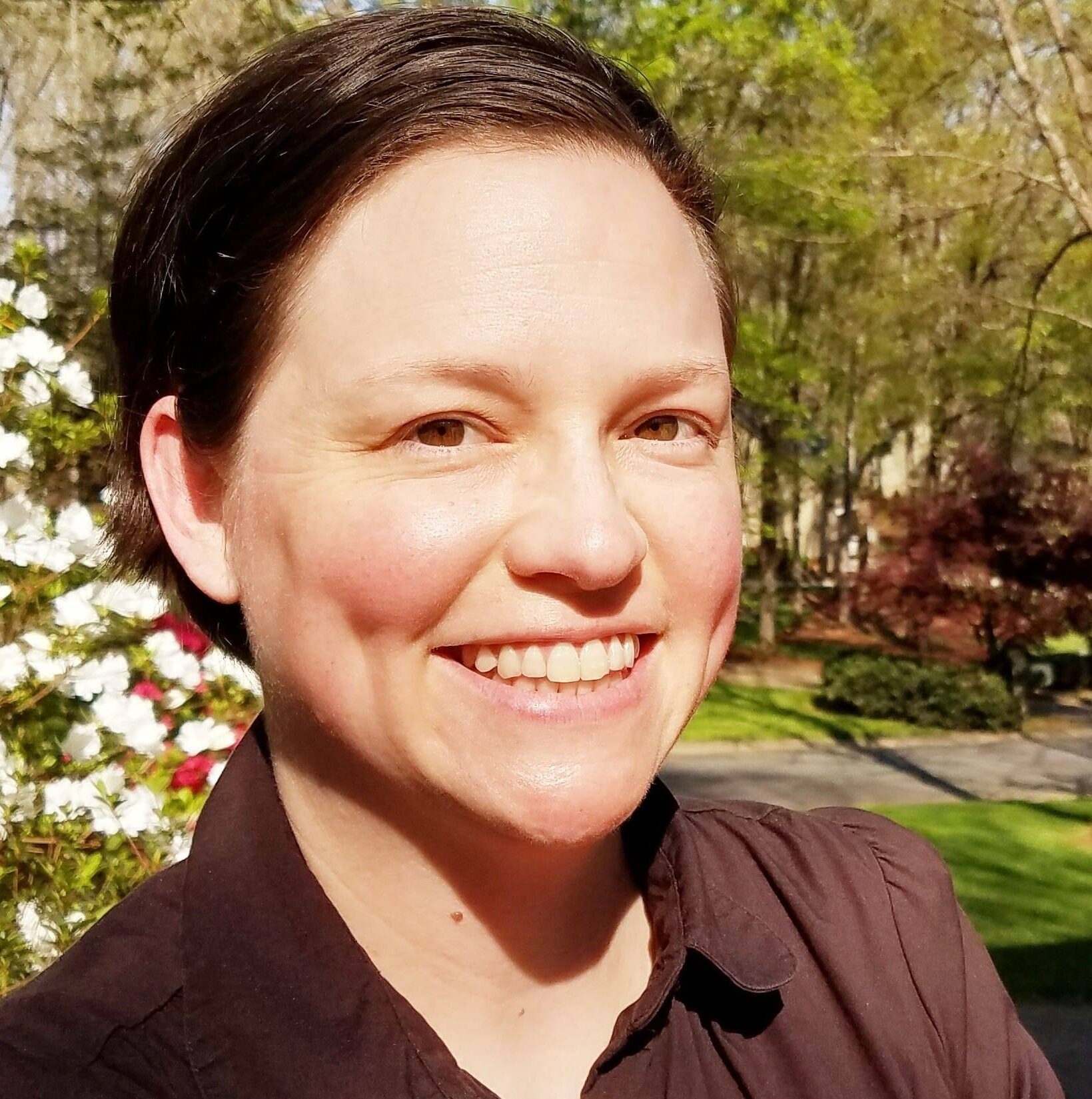 Image of author outside with white azalea blossoms and trees behind her.